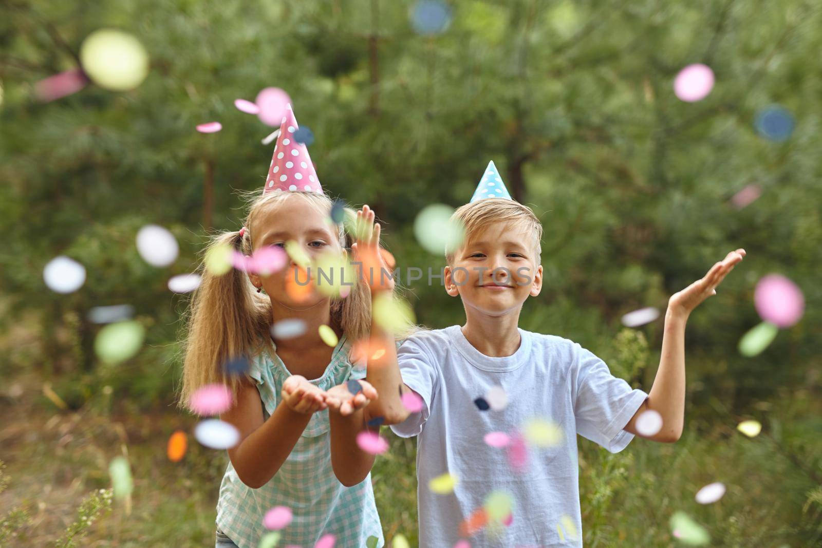 Little Girl and boy having fun celebrating Birthday while blowing confetti at party outdoor - Selective Focus
