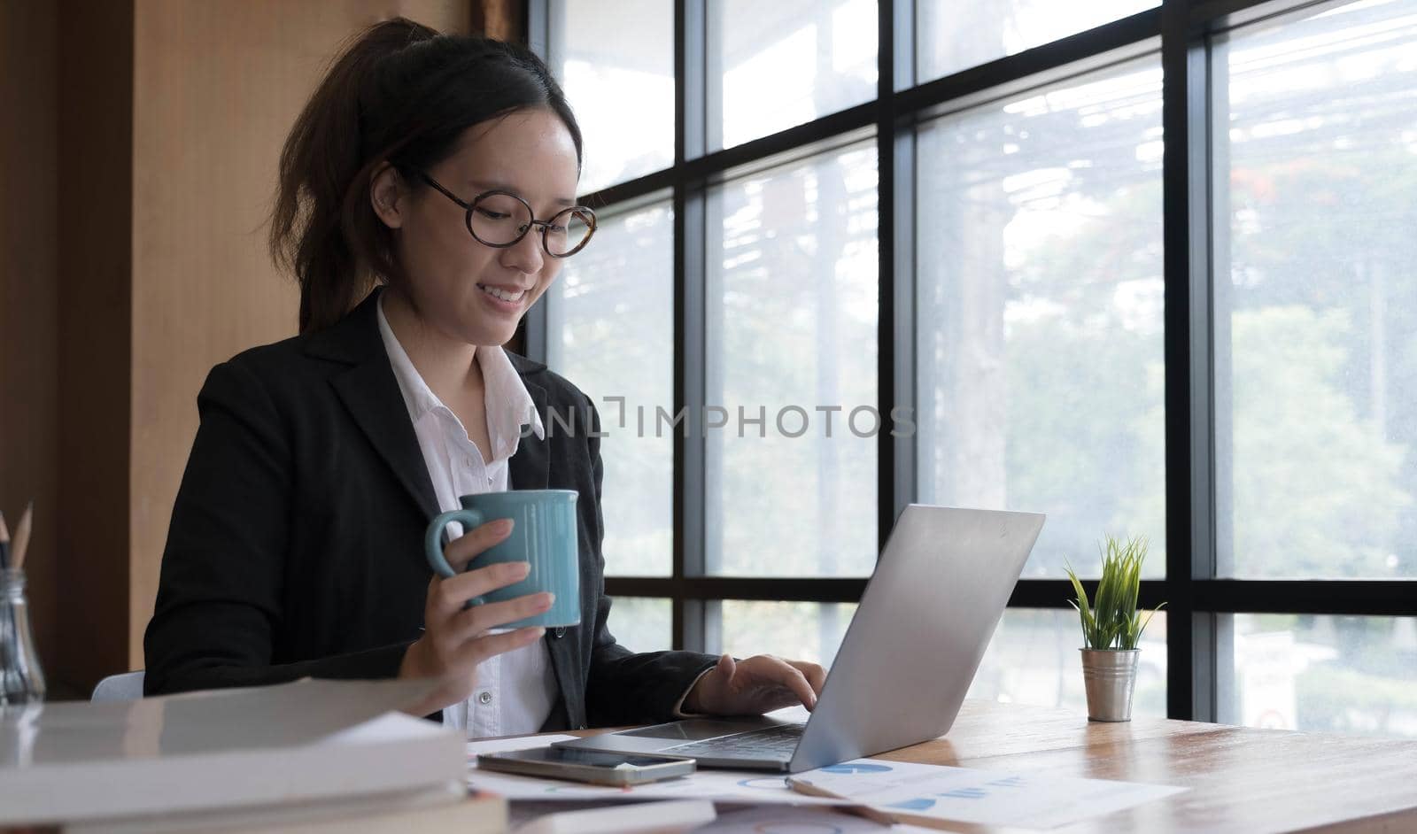 Young asian businesswoman have the pleasure of watching work on their tablet and favorite coffee at the office. by wichayada