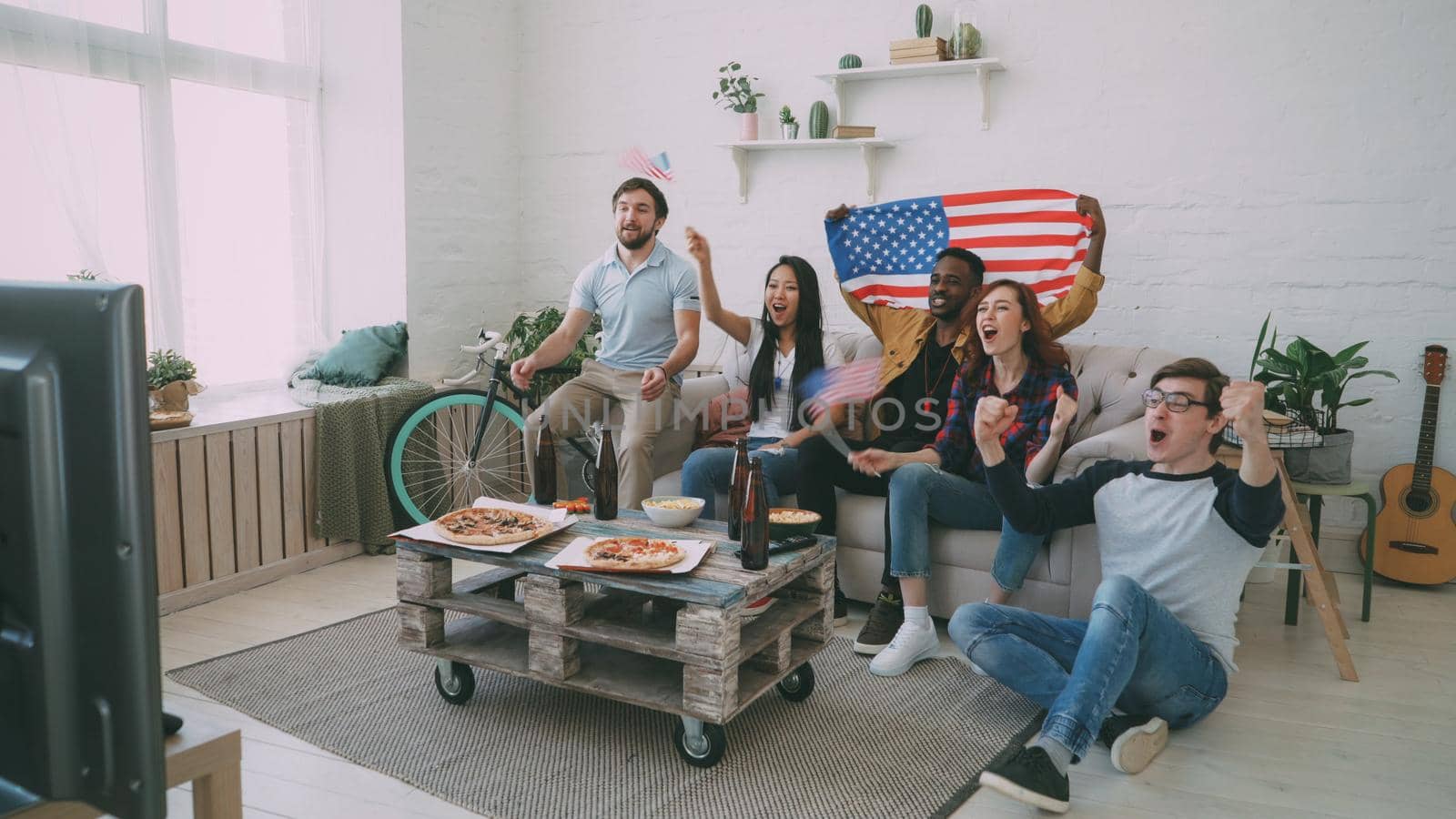 Multi ethnic group of friends with USA national flags watching sport championship on TV together cheering up their favourite team at home by silverkblack