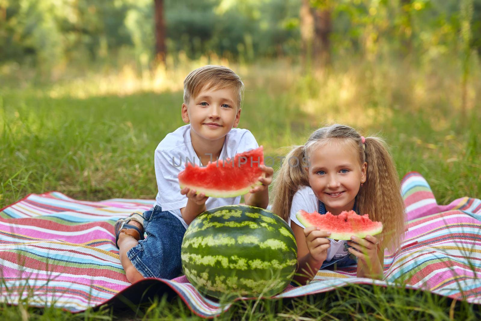 Cute kids eating watermelon in the garden. by InnaVlasova