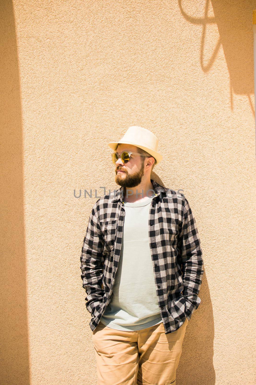 Fashion millennial stylish man posing on streets of european city. Bearded handsome hipster man posing near wall with hard shadows on hot noonday - summer vacations and holiday concept by Satura86
