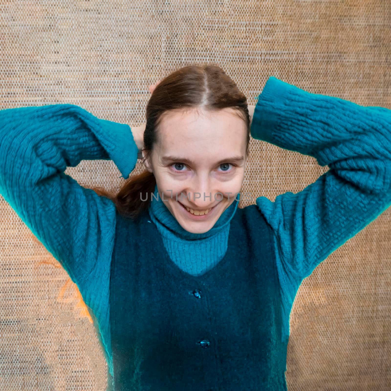 a red-haired girl in a green warm suit against a straw wall smiles and straightens her hair