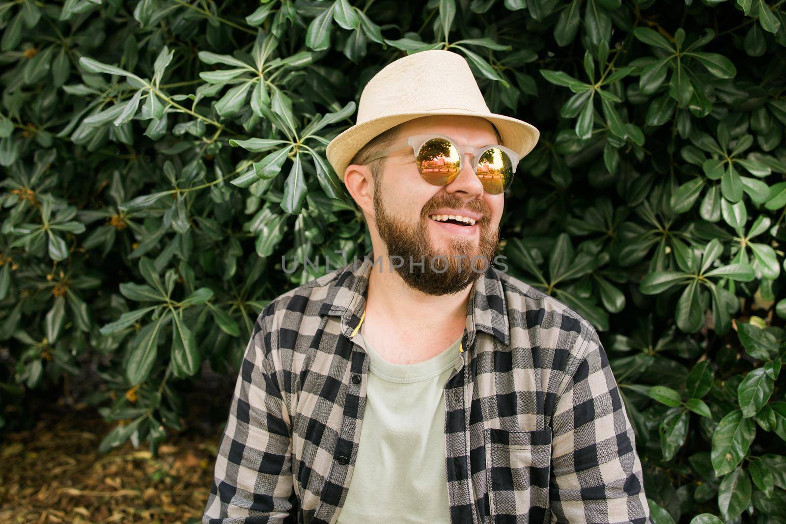 Laughing attractive man wearing hat over green tree background - emotion and vacation travel holidays