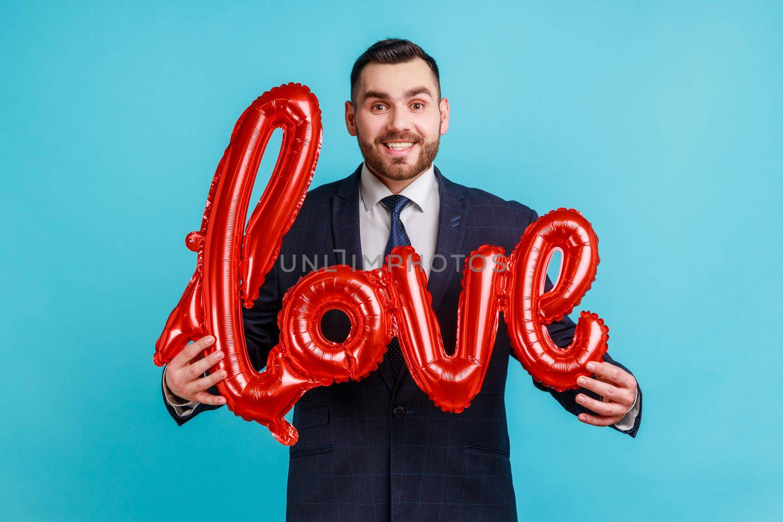 Portrait of happy smiling man wearing official style suit holding love word of foil balloons, expressing positive emotions and his feelings. by Khosro1