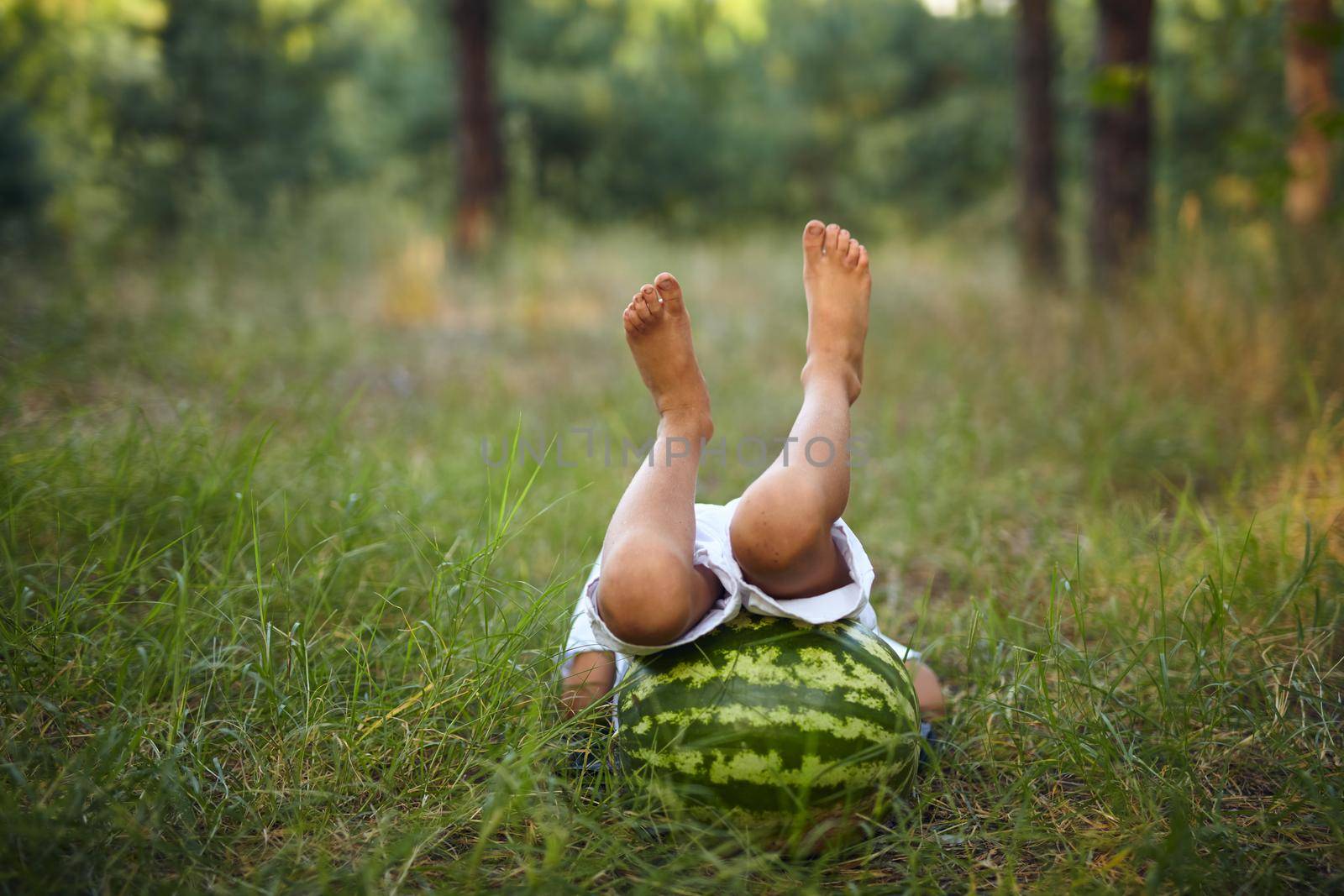 Funny photo of a boy lying on a large watermelon with his feet up. Pampering, fun, harvest, childhood concept