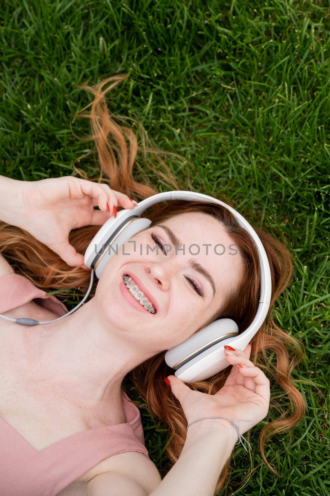 A young red-haired woman lies on the grass and listens to music. by mrwed54