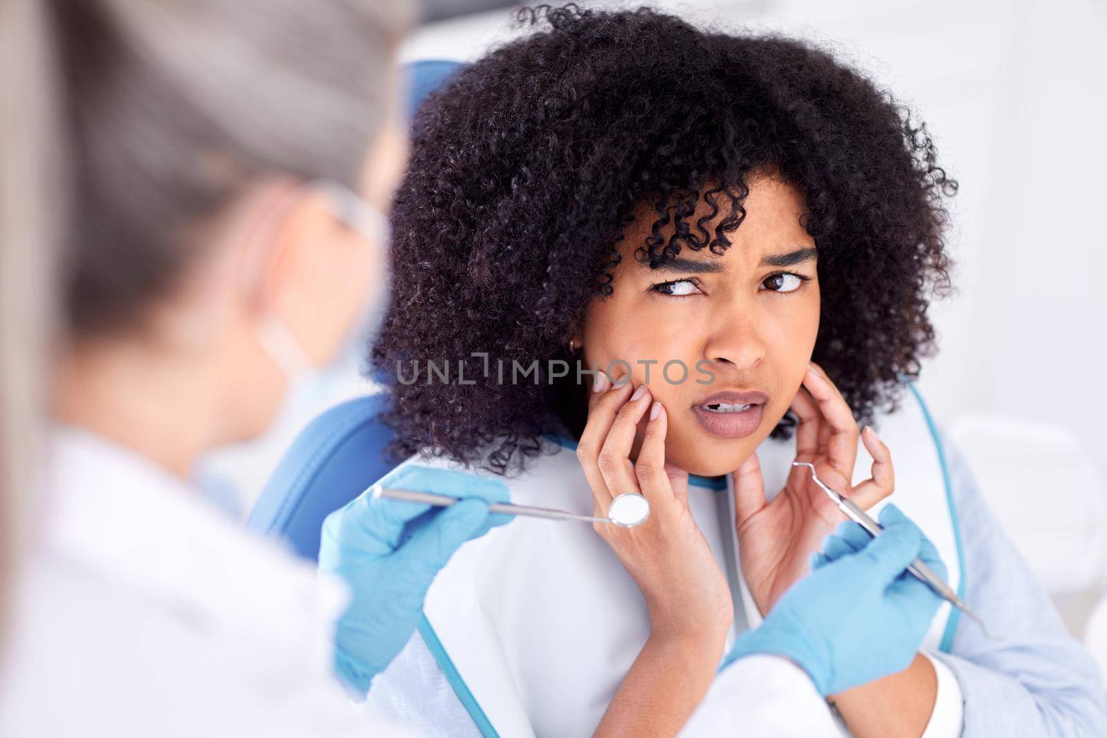 Shot of a young woman experiencing pain and anxiety while having a dental procedure performed on her.