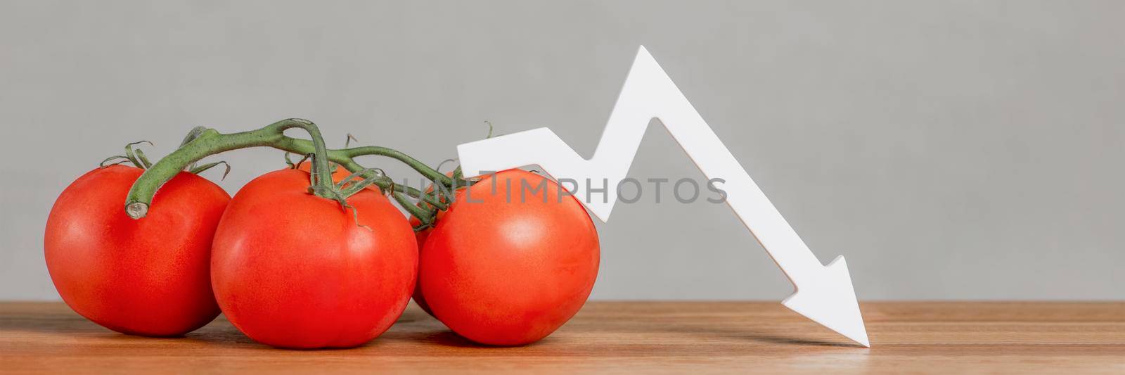 The price of tomatoes and vegetables. Bad vegetable harvest. Fresh red ripe tomatoes with twigs on the table. Graph chart points down. by SERSOL