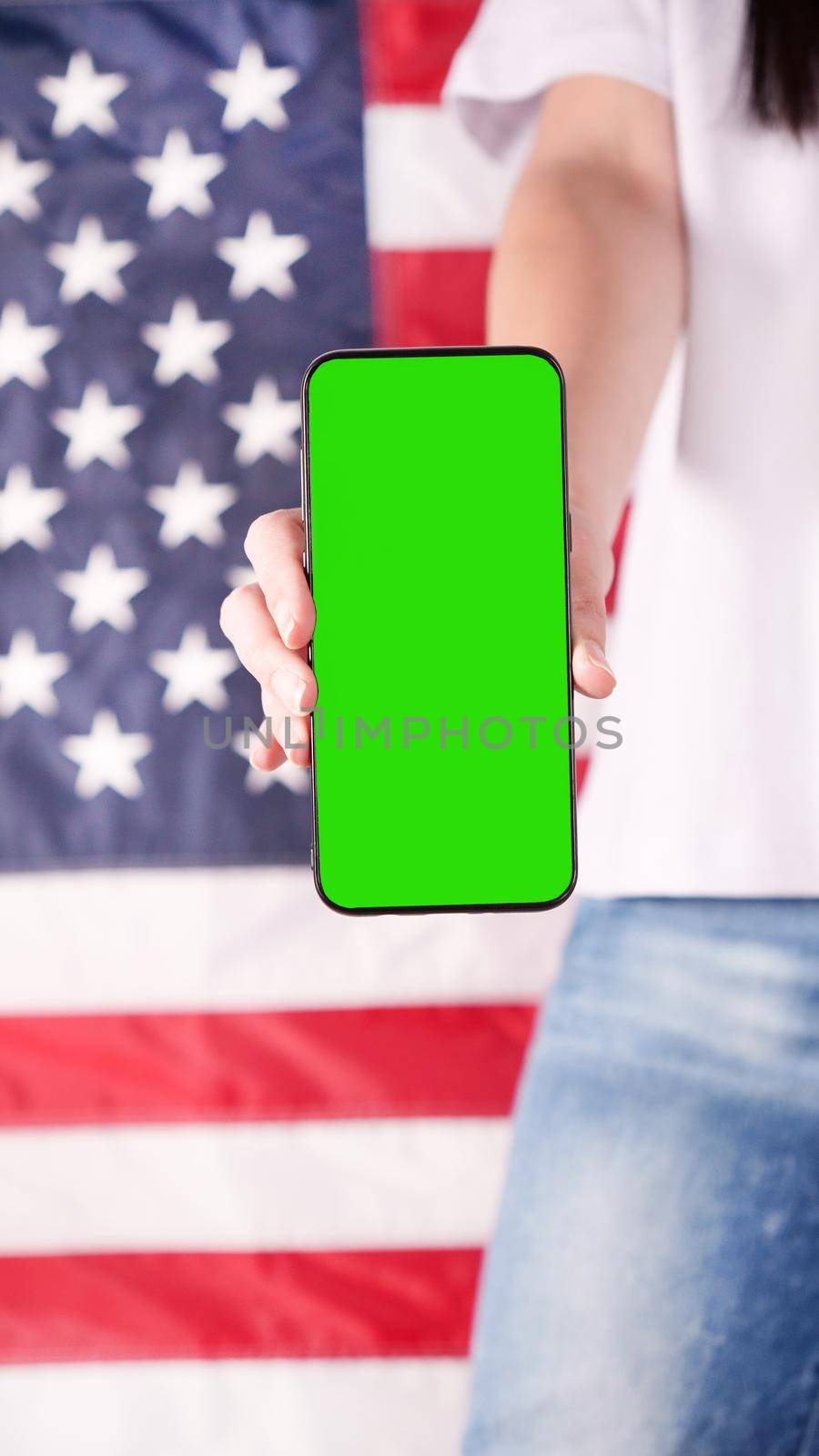 Hand holding mobile phone with green screen United states of America flag on background. Mockup phone. Labor day, 4th of July, Memorial day, 9.11