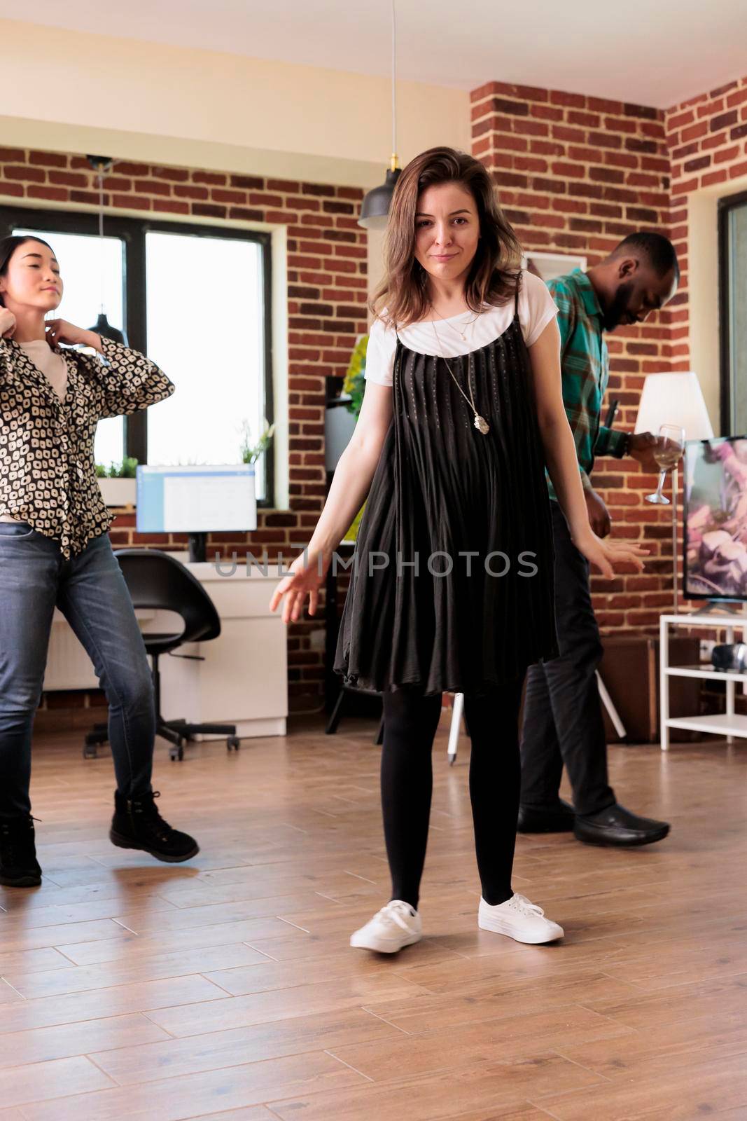 Diverse group of young people dancing in living room at wine party while celebrating birthday. Cheerful friends having celebration event for friendship anniversary while drinking alcoholic beverages.