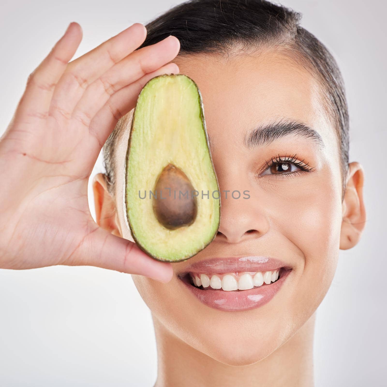 Feed your skin what it needs. Studio shot of a young woman posing with half an avocado against a grey background. by YuriArcurs