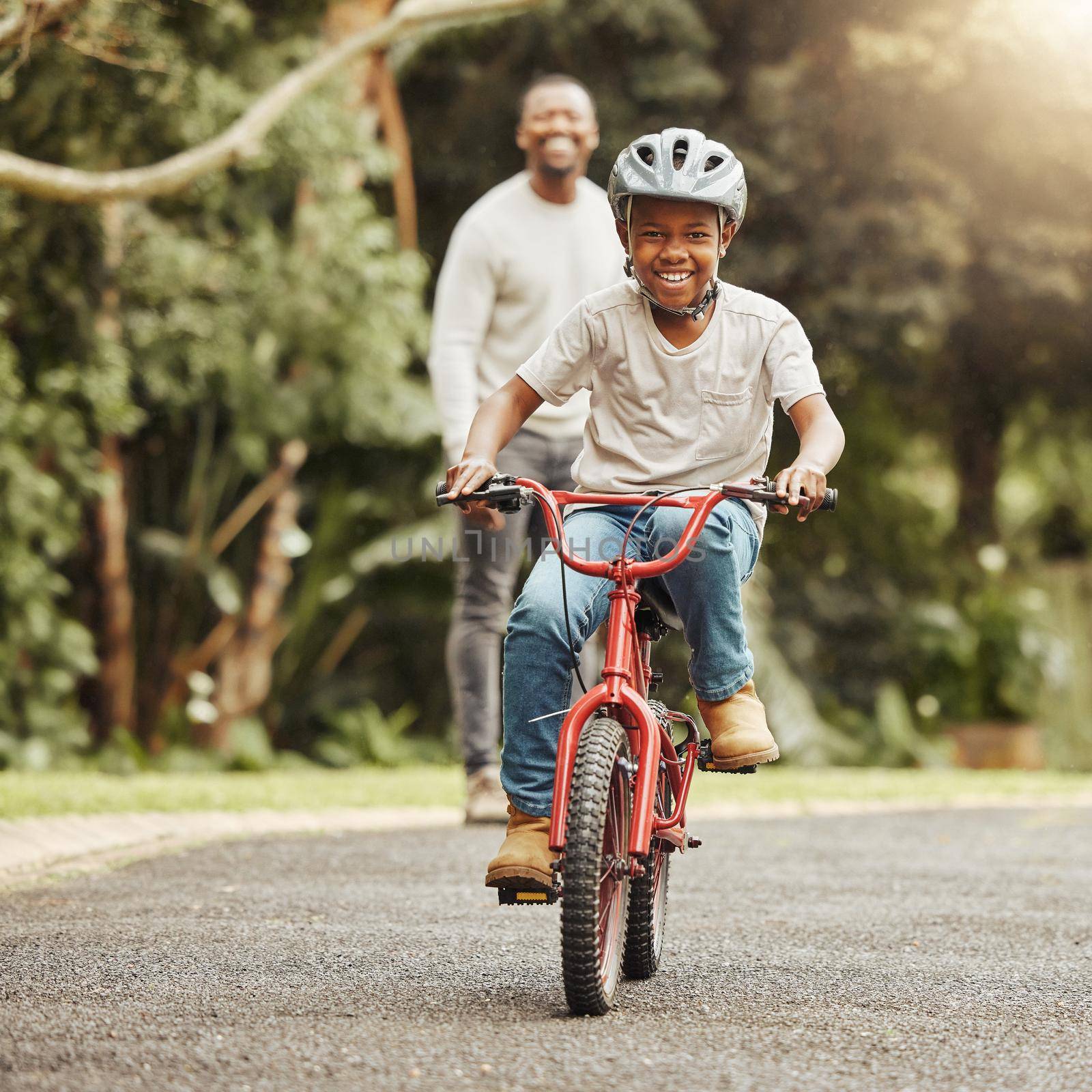 Look at him go. Shot of an adorable boy learning to ride a bicycle with his father outdoors. by YuriArcurs