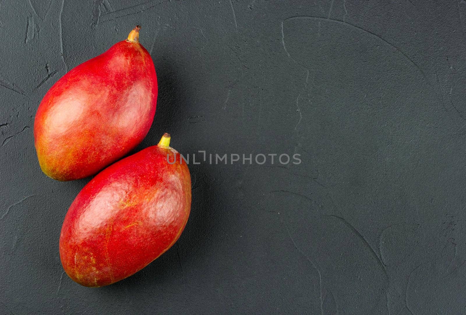 Two red delicious mango fruits on a concrete background, top view