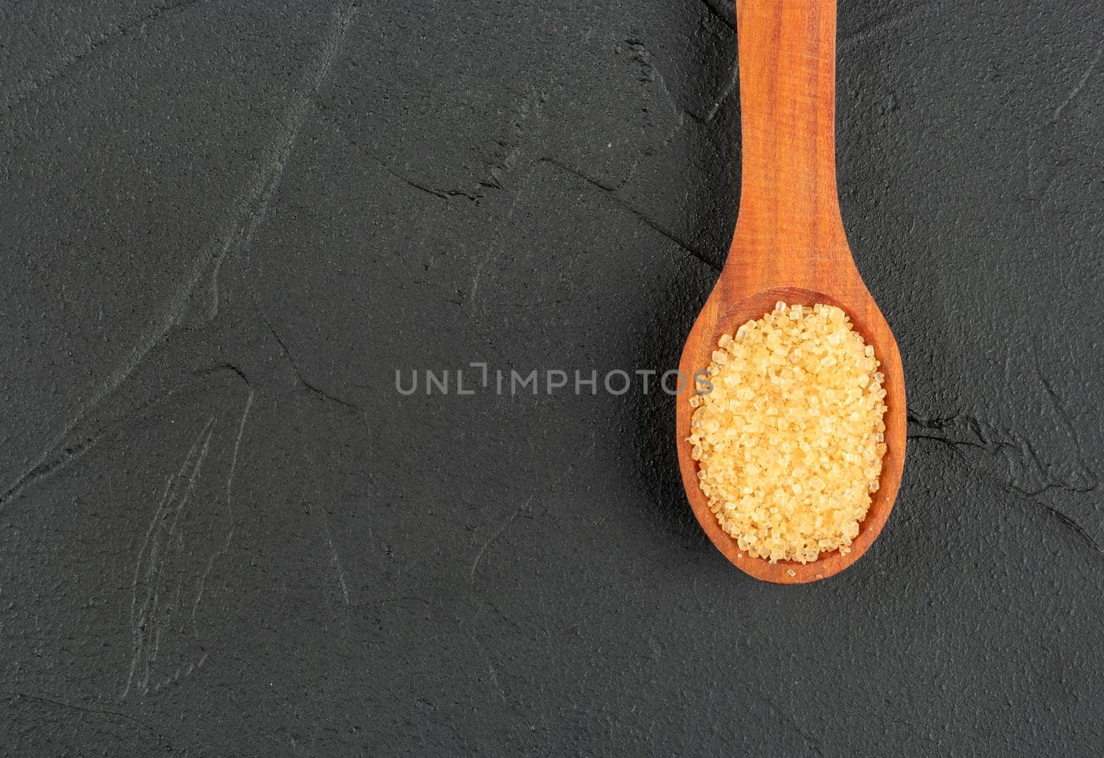 Brown sugar in a wooden spoon close-up on a dark background, top view