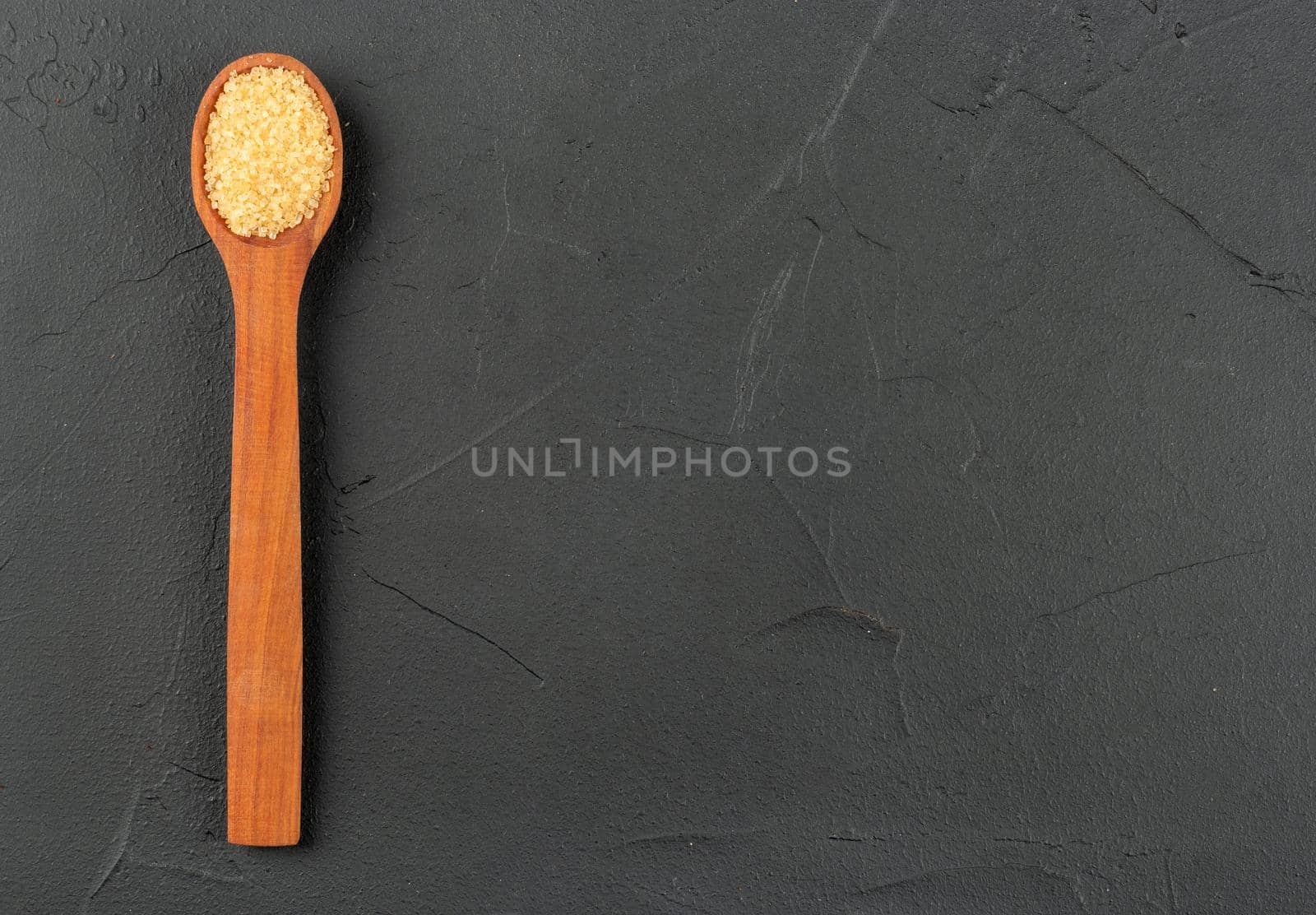 Wooden spoon with brown sugar on empty concrete background