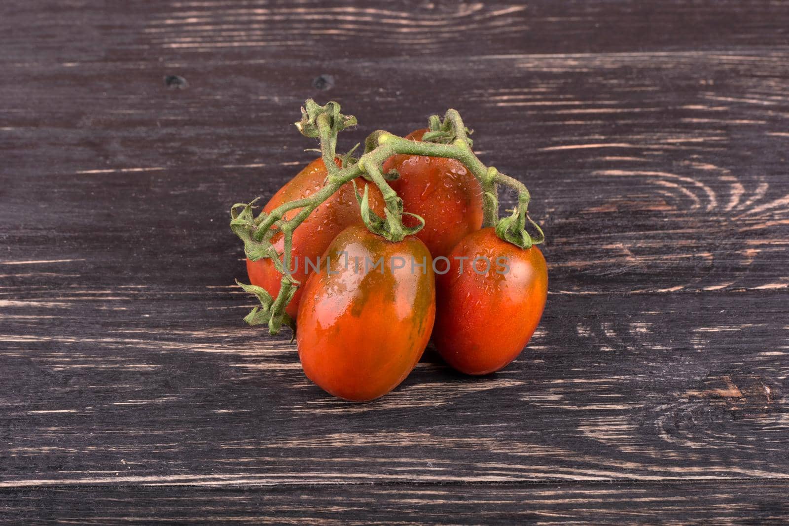 Sprig of red four tomatoes with drops on a dark wooden background