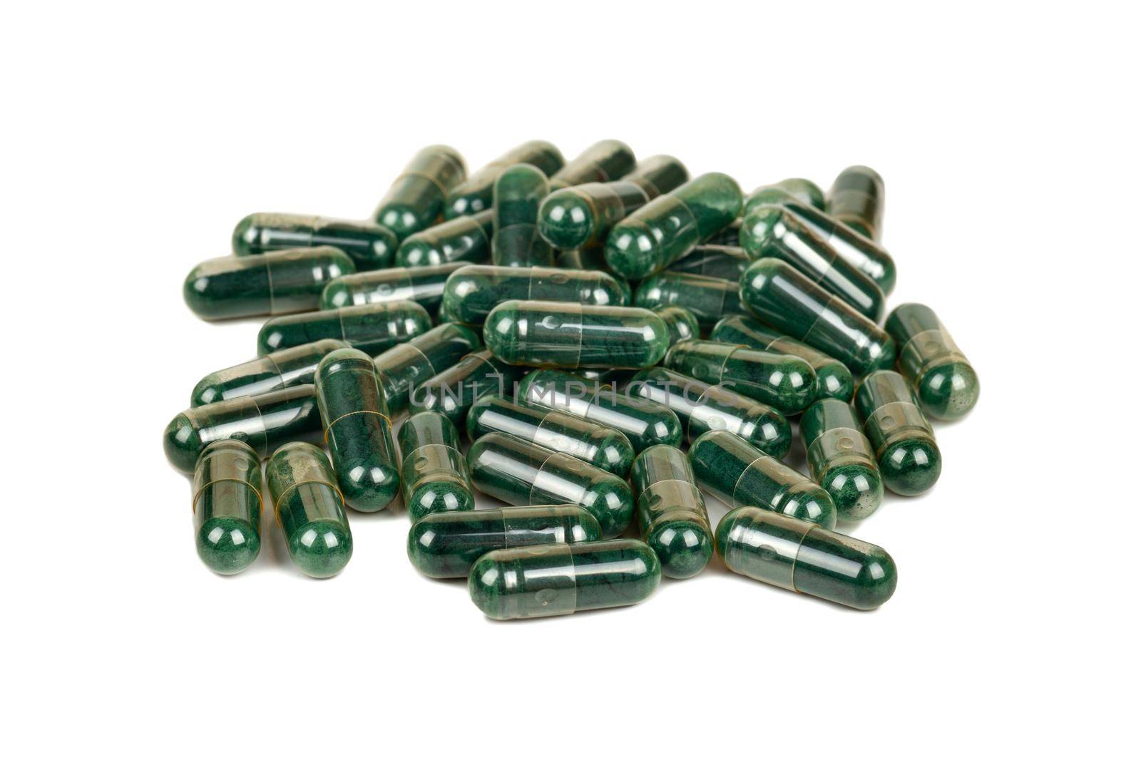 Pile of green capsules with medicinal herbs on a white background