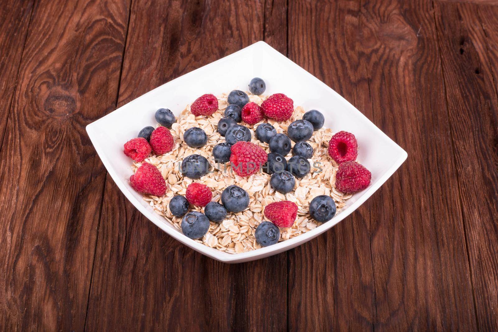 White bowl full of oatmeal with raspberries and blueberries on a wooden table