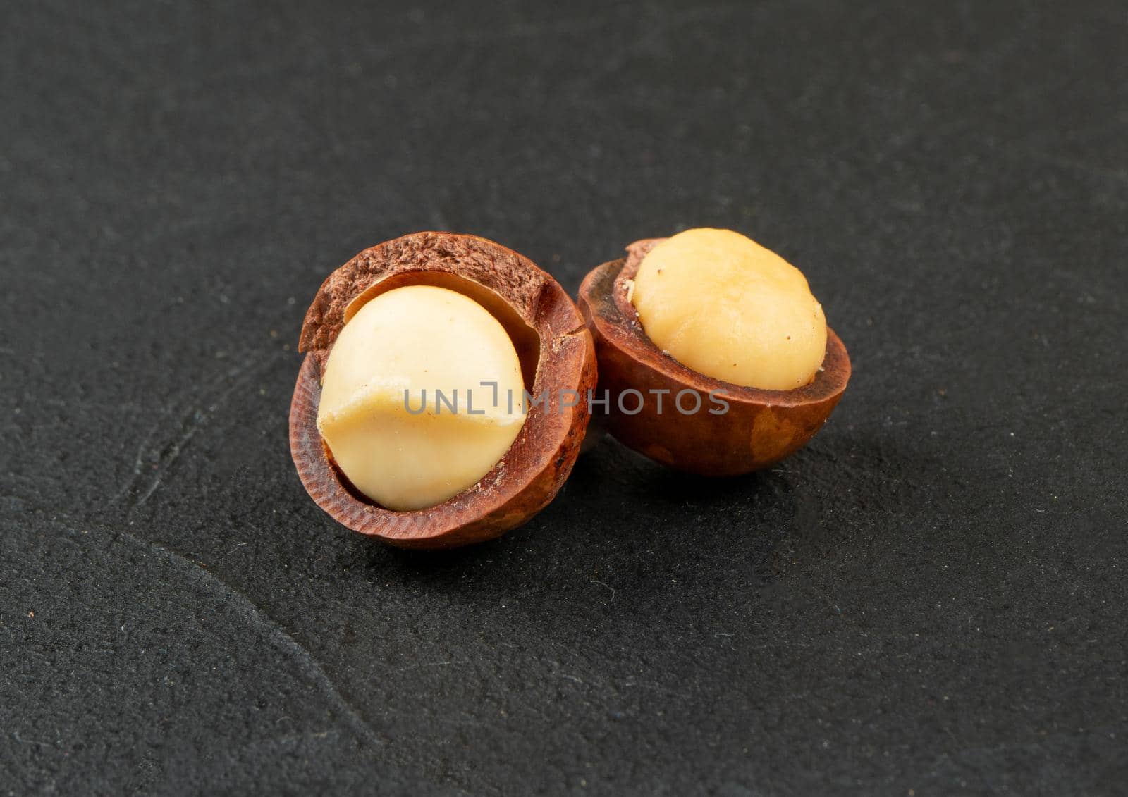 Two open macadamia nuts on a dark concrete background