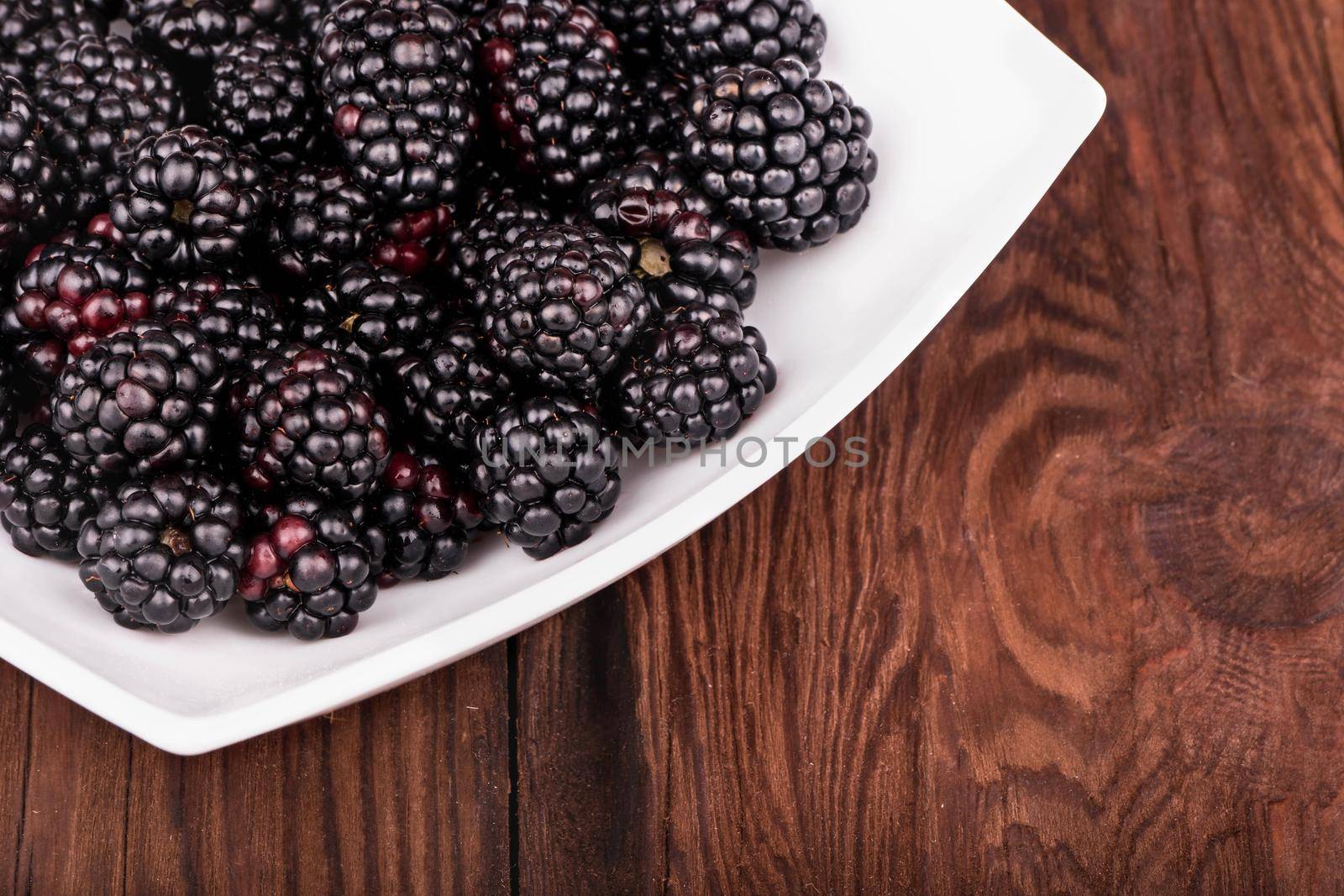 Part of a white bowl with blackberries close-up on a brown wooden table