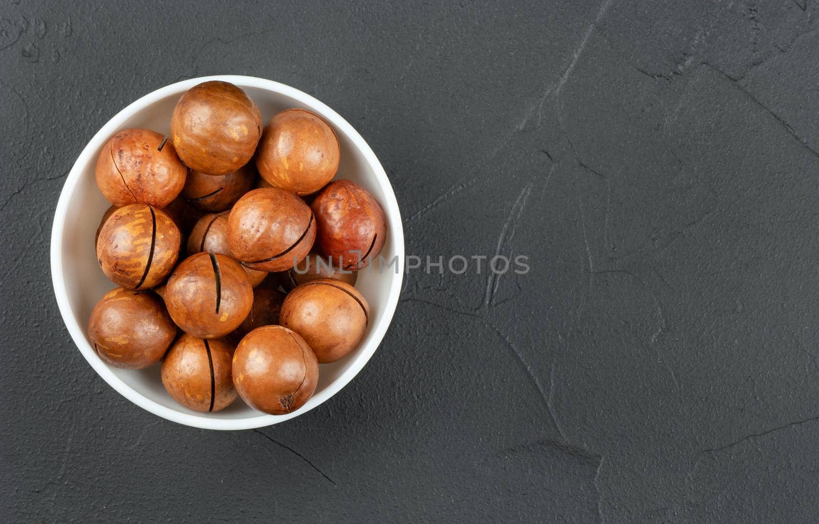 Macadamia nuts in a white bowl on an empty concrete dark background