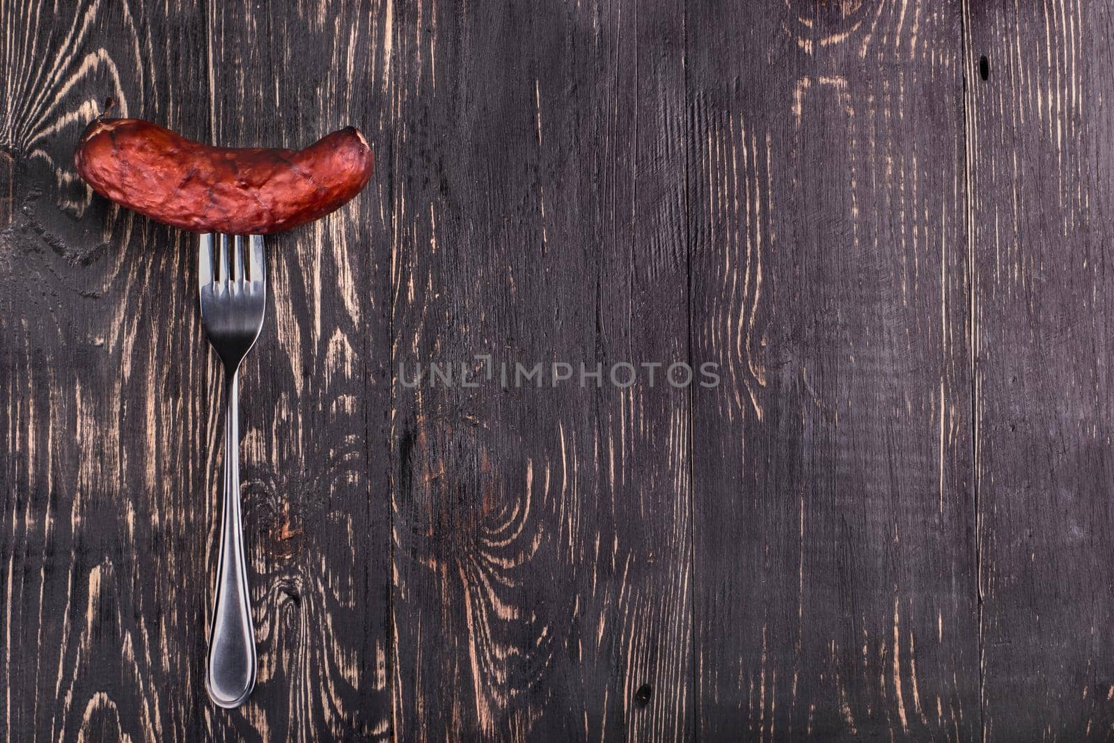 Meat sausage for grilling on a fork on a dark wooden background