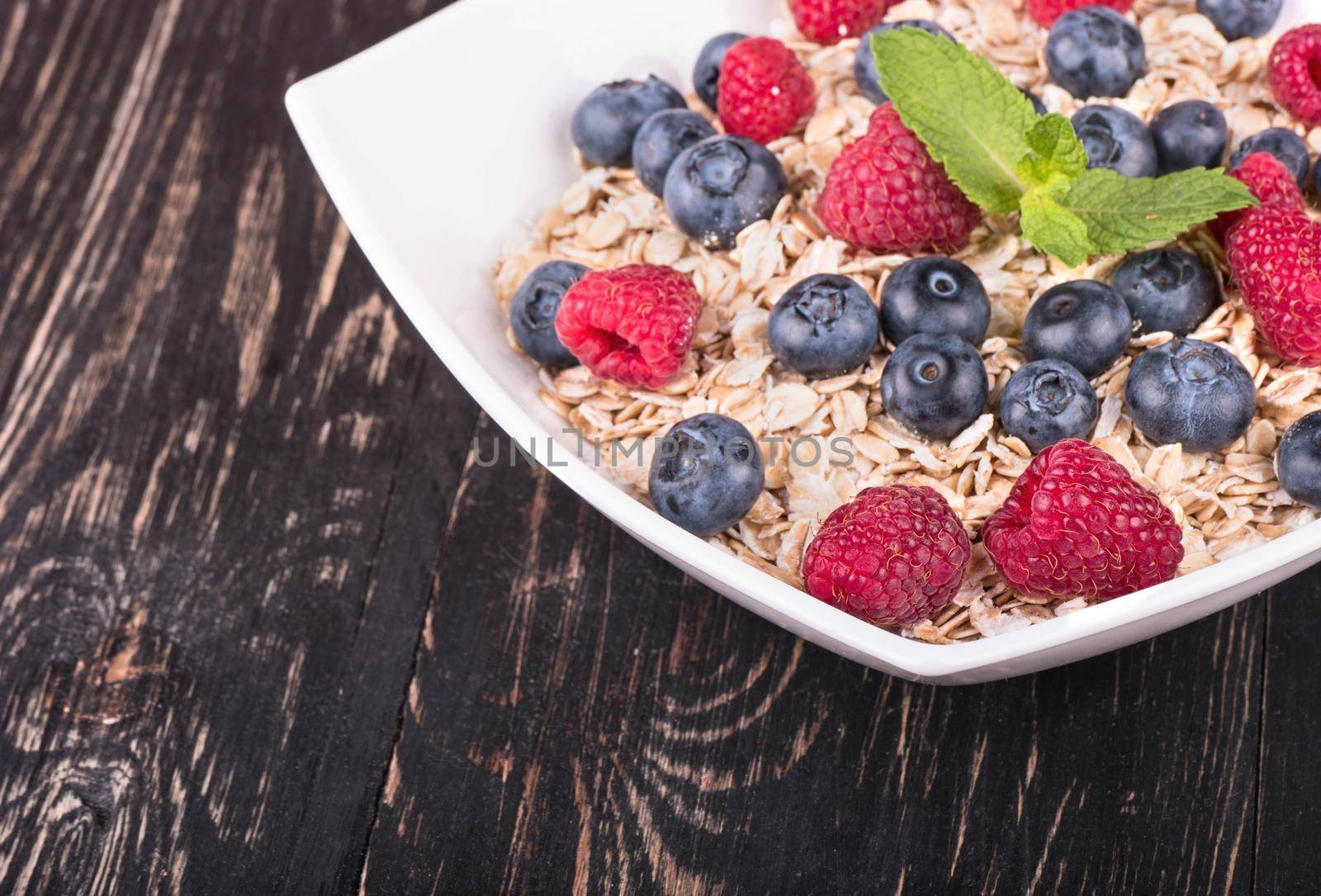 Part bowls filled with oatmeal and raspberries and blueberries on a dark wooden background