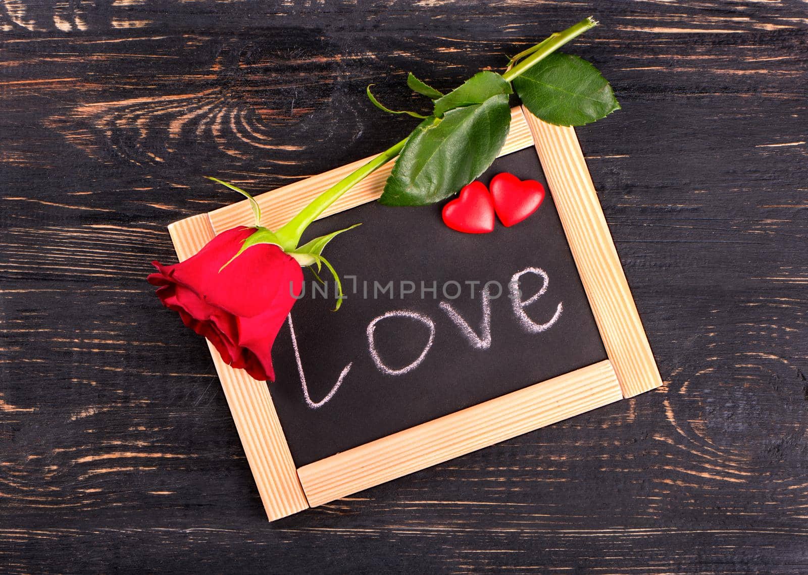 Board with the word love, red rose and hearts symbolizing valentines day top view