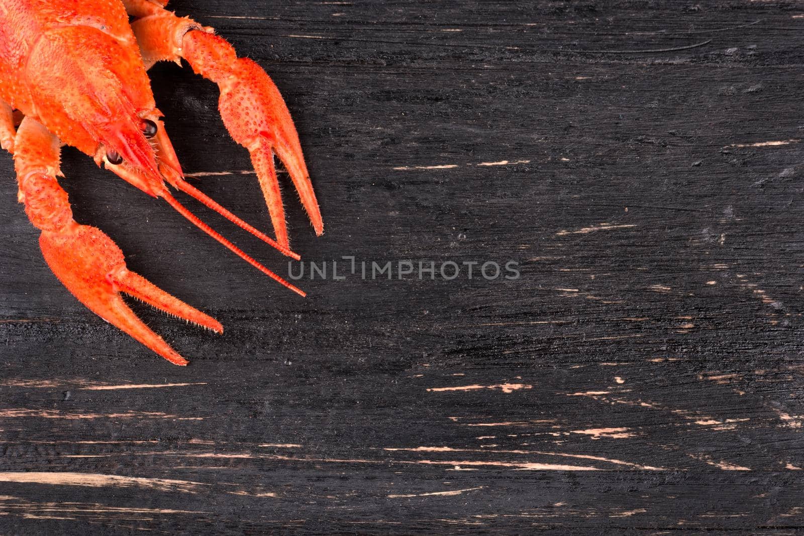 Red boiled crawfish is located in the corner of a dark wooden table