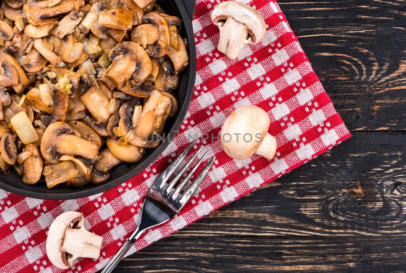 Part of the frying pan with fried mushrooms champignon and fork on a towel, a top view