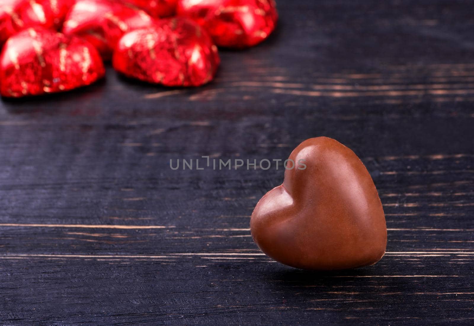 Several chocolate candies in foil and shape of the heart on a dark wooden table