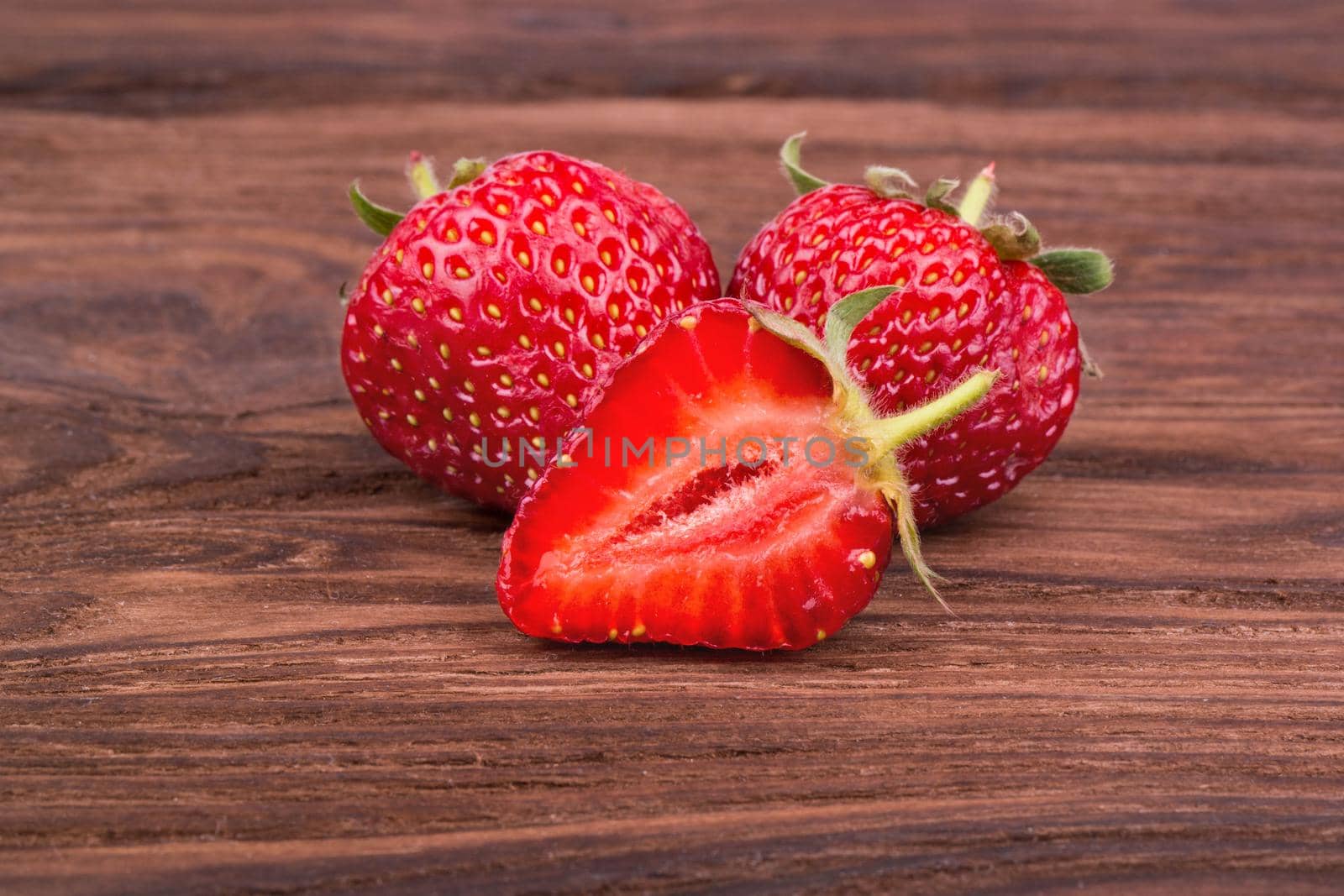 Two fresh ripe strawberries with sliced half on a wooden background