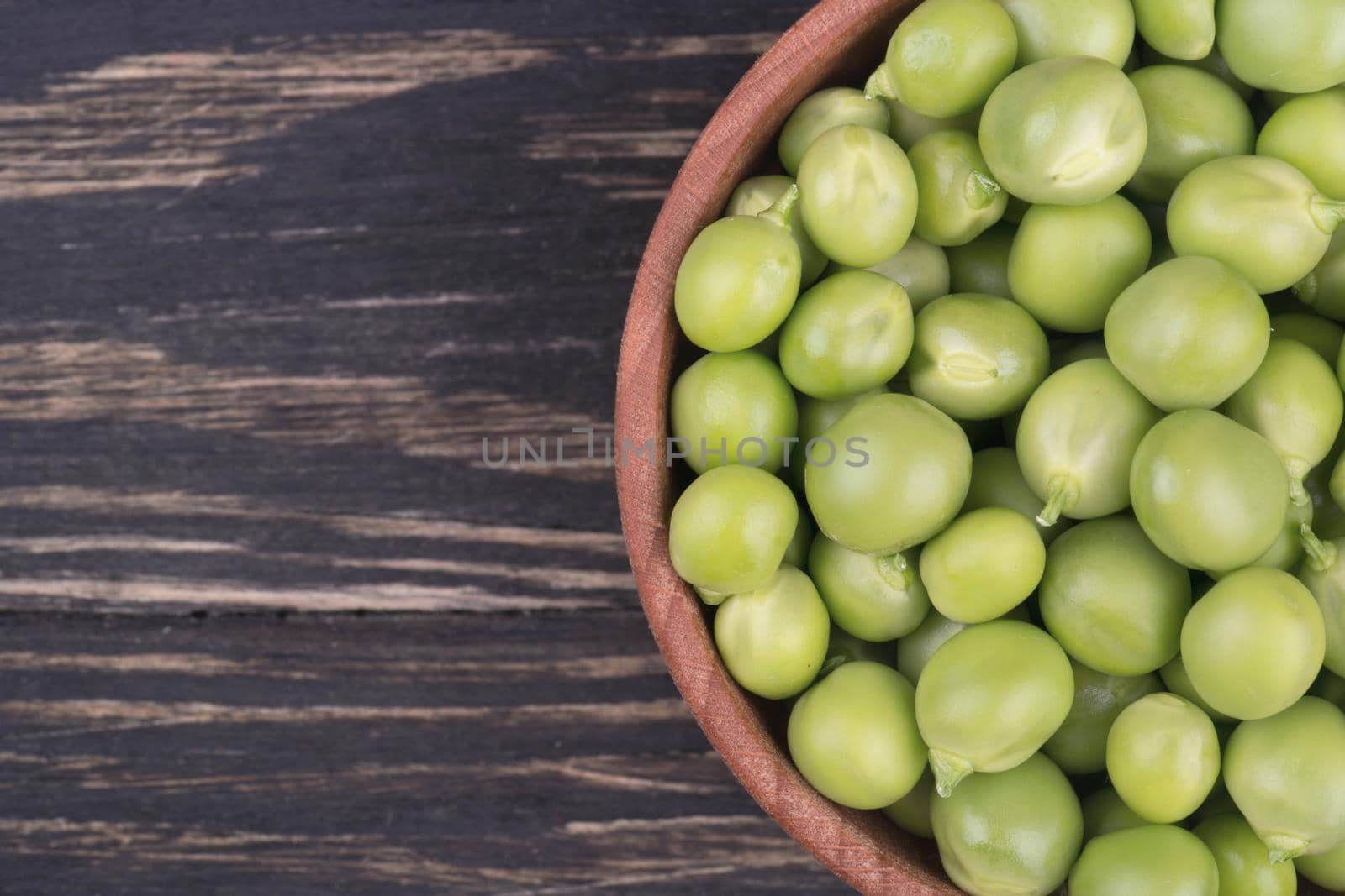 Fresh green peas in a wooden bowl on a wooden background top view