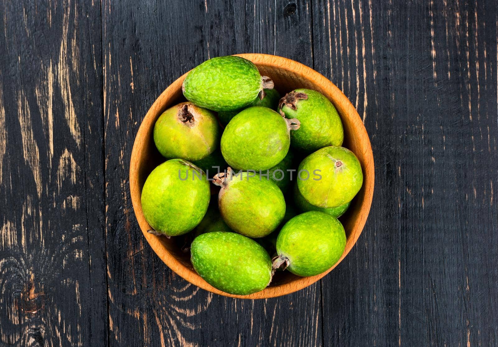 Wooden bowl filled with fresh fruit feijoa on the table top view