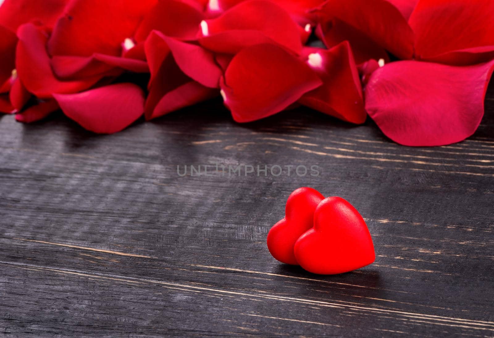 Two hearts on a wooden background with scattered red rose petals