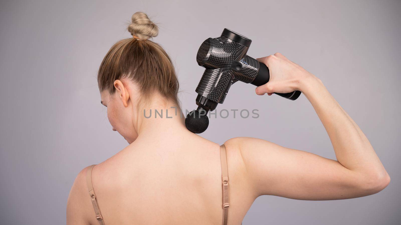 Caucasian woman giving herself a back massage with a gun