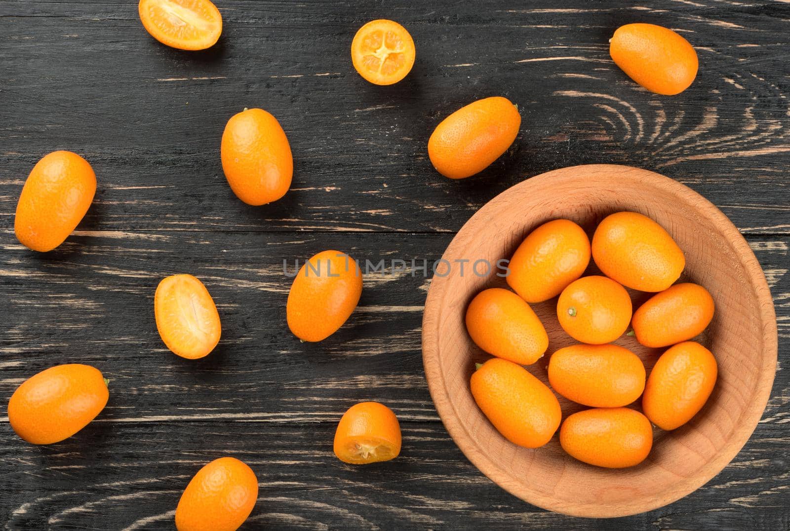 Bowl with kumquat and scattered fruit on wooden background, top view