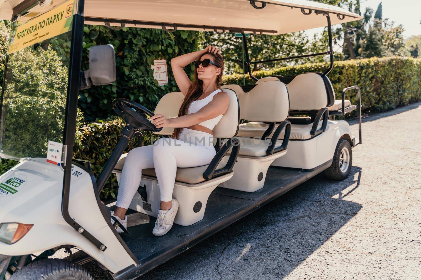A middle-aged woman is driving a car for transporting tourists. Electric car, Tourist bus. Car for transporting people around the hotel, park, golf club.