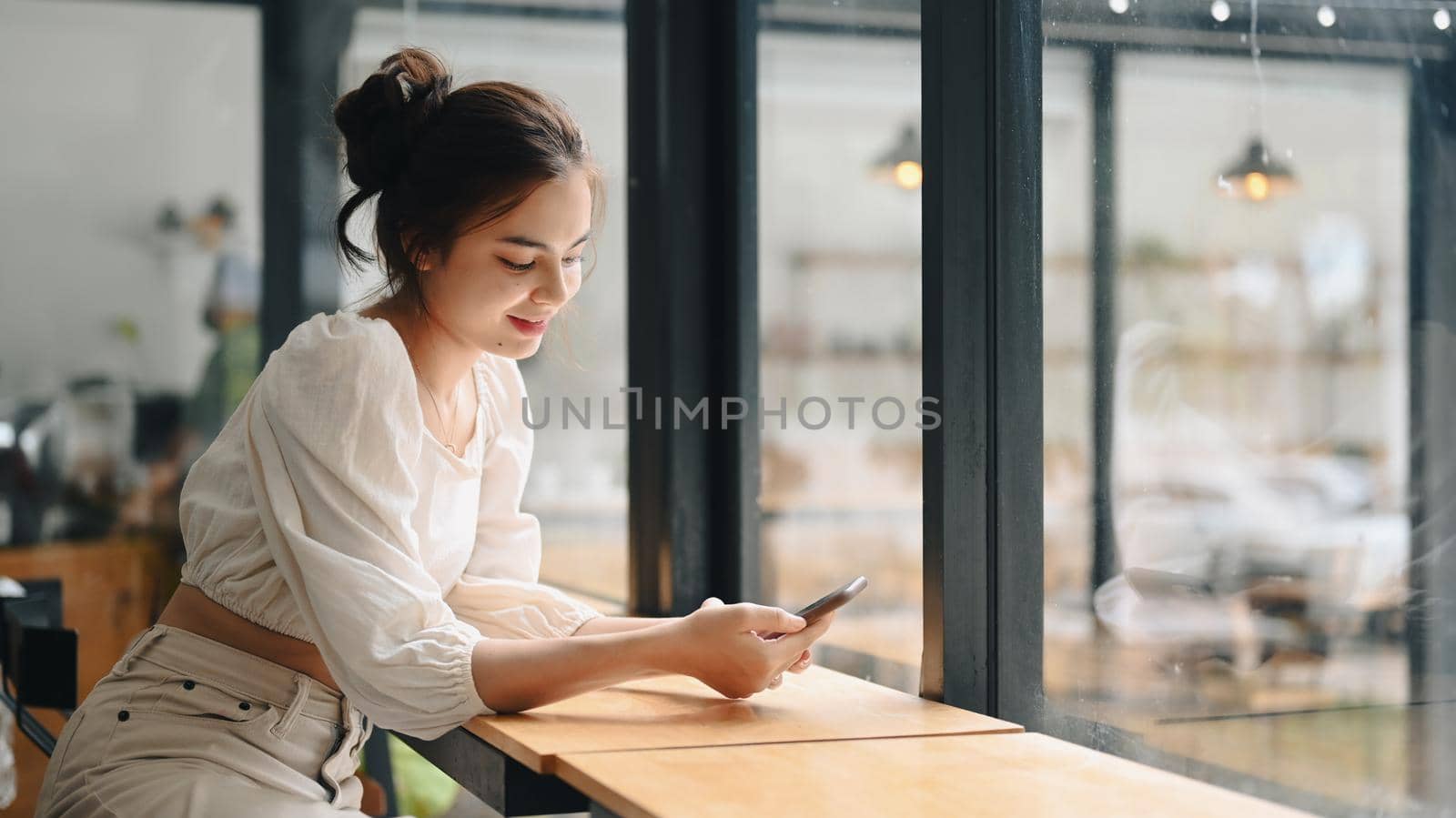 Young woman sitting at modern coffee shop and chatting online in social network on smart phone.