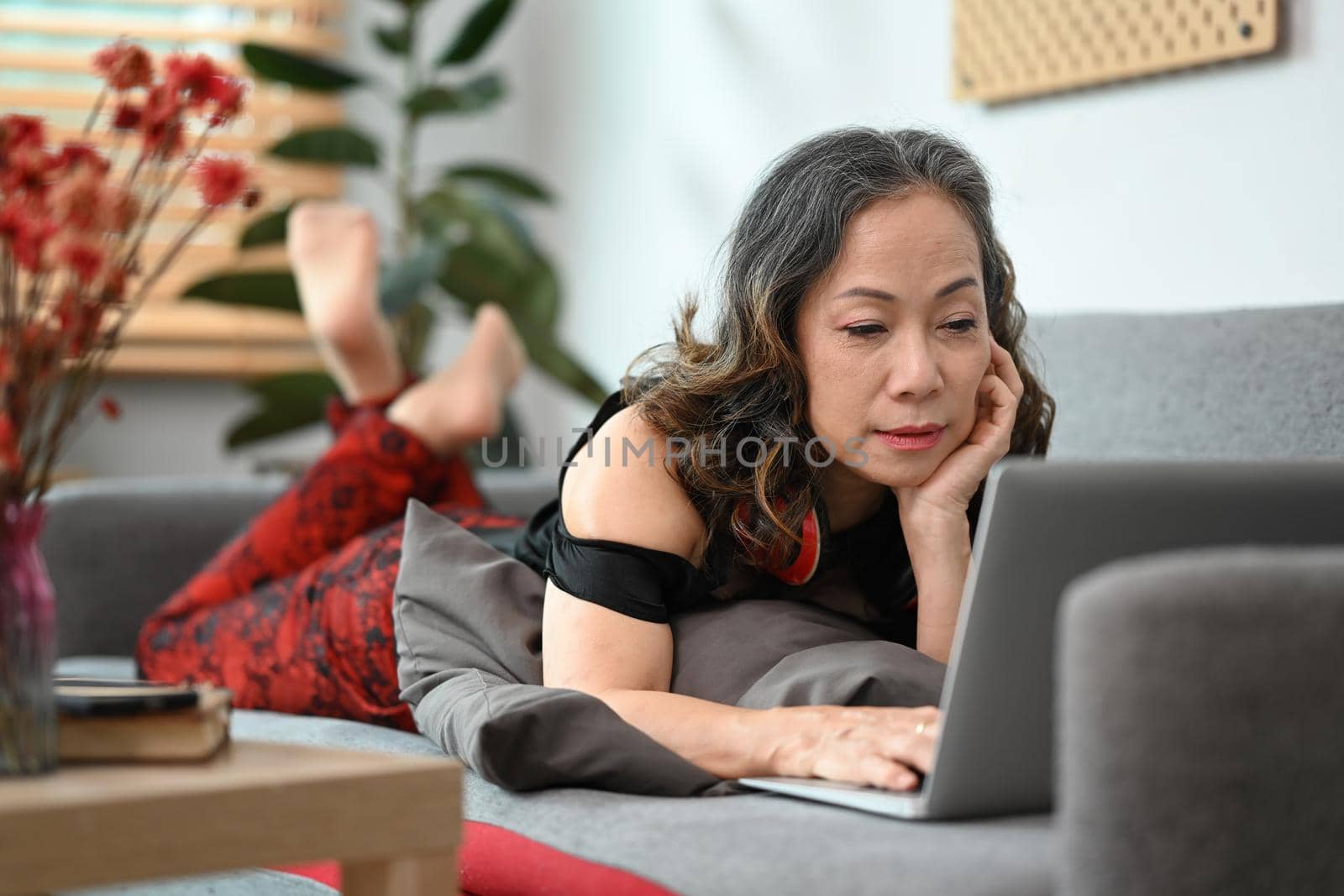 Middle aged woman lying on comfortable sofa and using laptop computer.