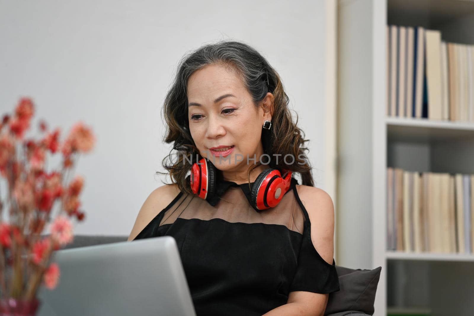 Relaxed middle aged lady surfing internet, watching video on laptop computer by prathanchorruangsak