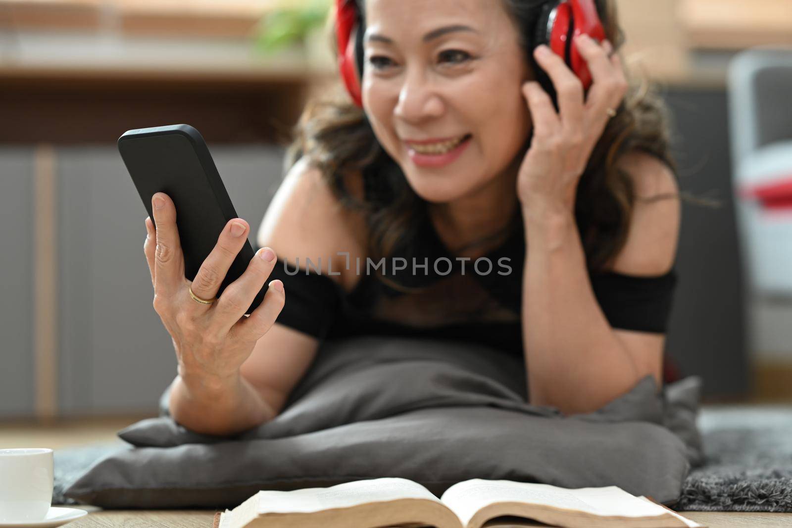 Happy mature woman wear wireless headphone and watching video on her mobile phone, relaxing at home.