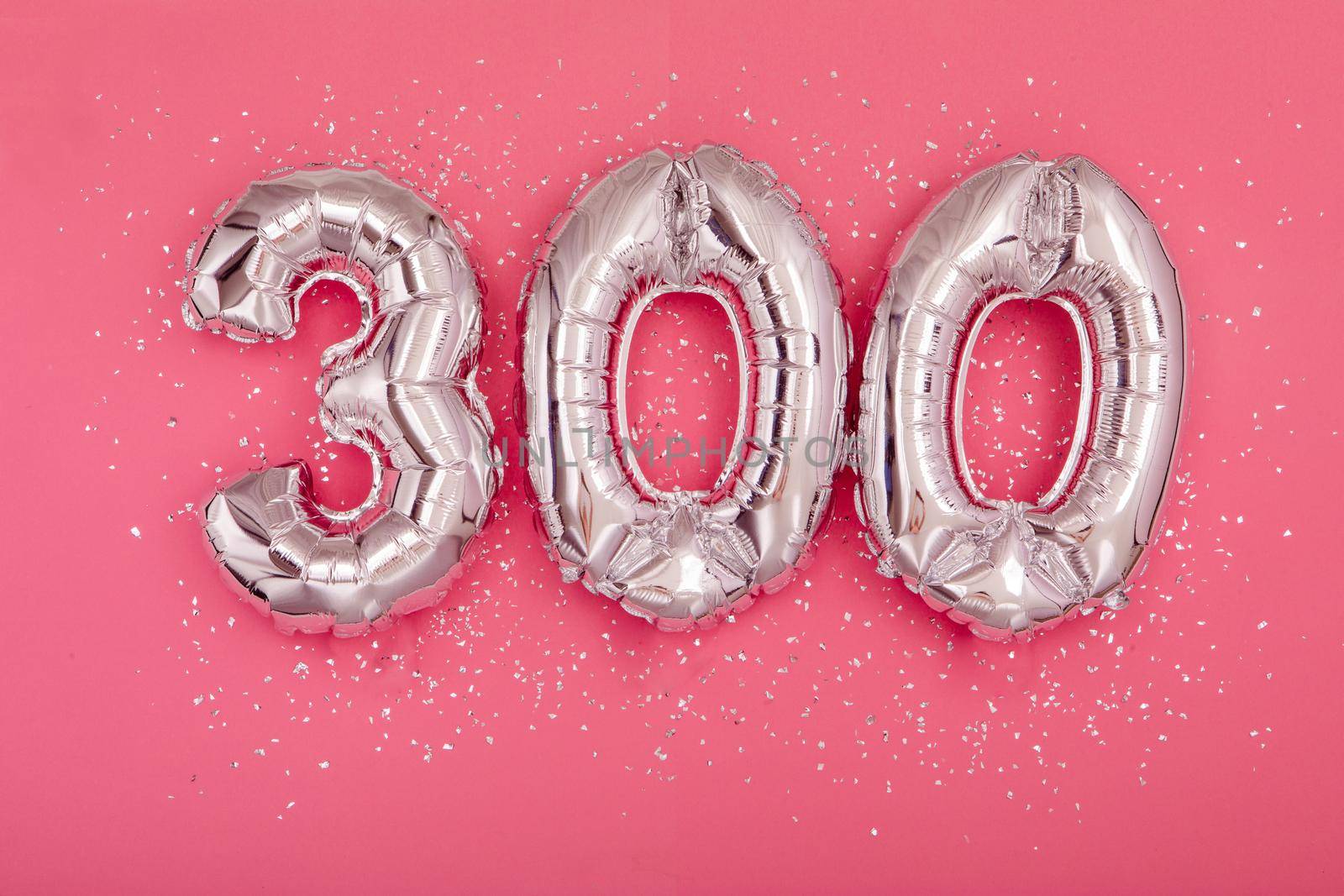From above of silver shiny balloons demonstrating number 300 three hundred pink background with scattered glitter