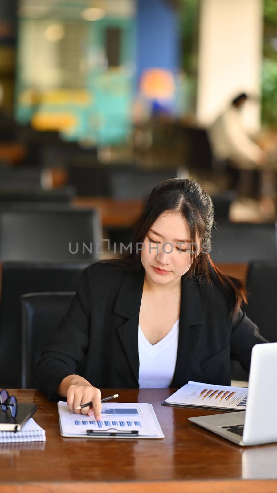 Portrait asian businesswoman analyzing graph and working with laptop at office desk.