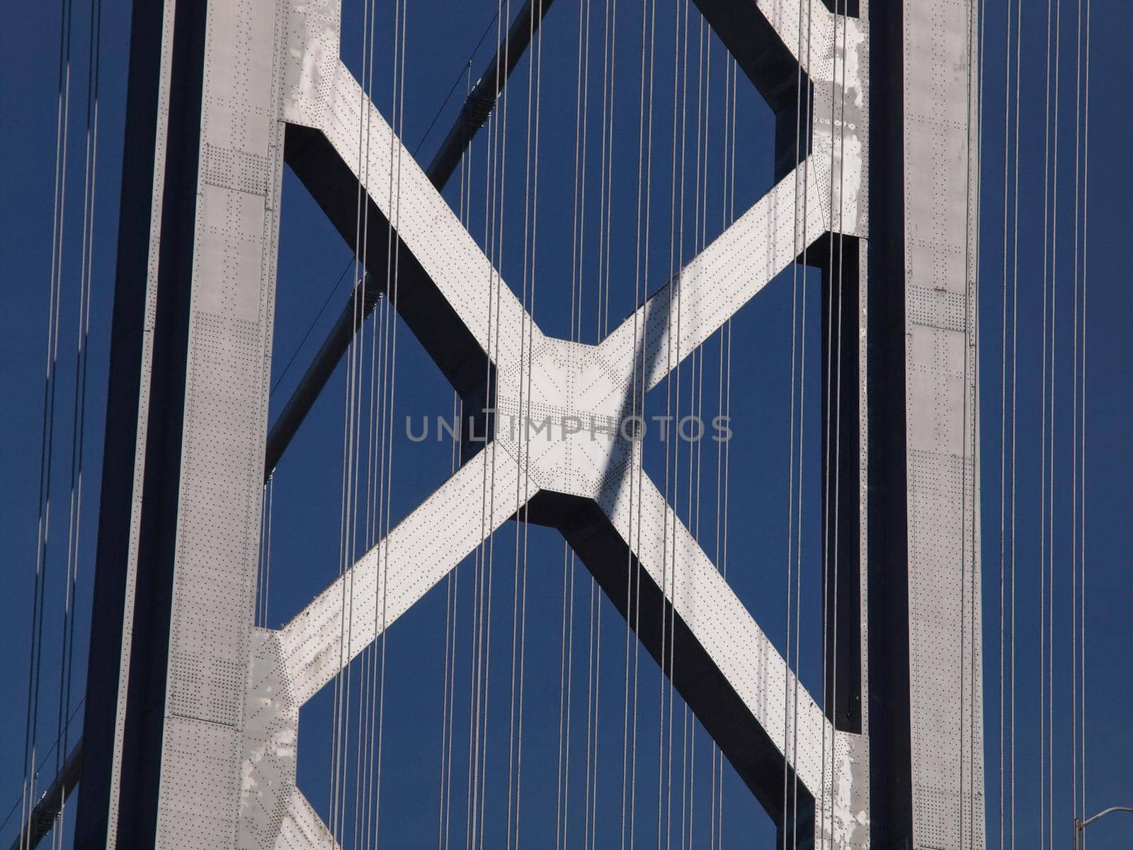 Close up of San Francisco Bay Bridge Tower above road and cables on a clear blue day.