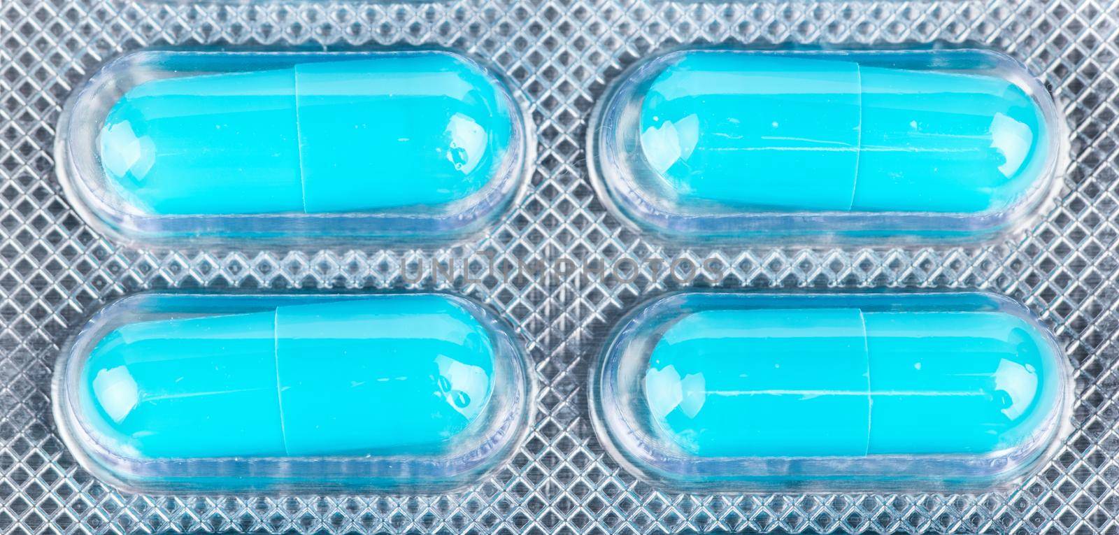 Four blue capsules in blister closeup