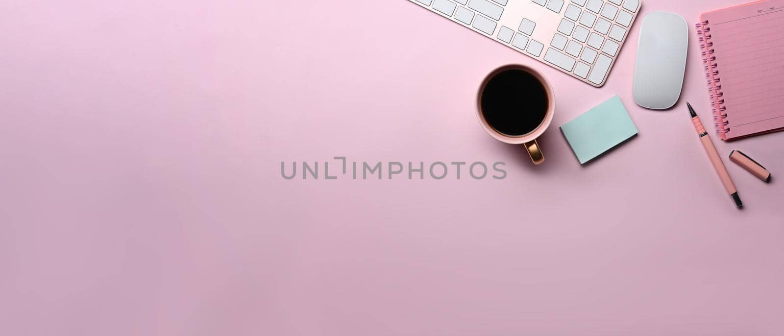 Female workspace with coffee cup, sticky note and notebook on pink background.