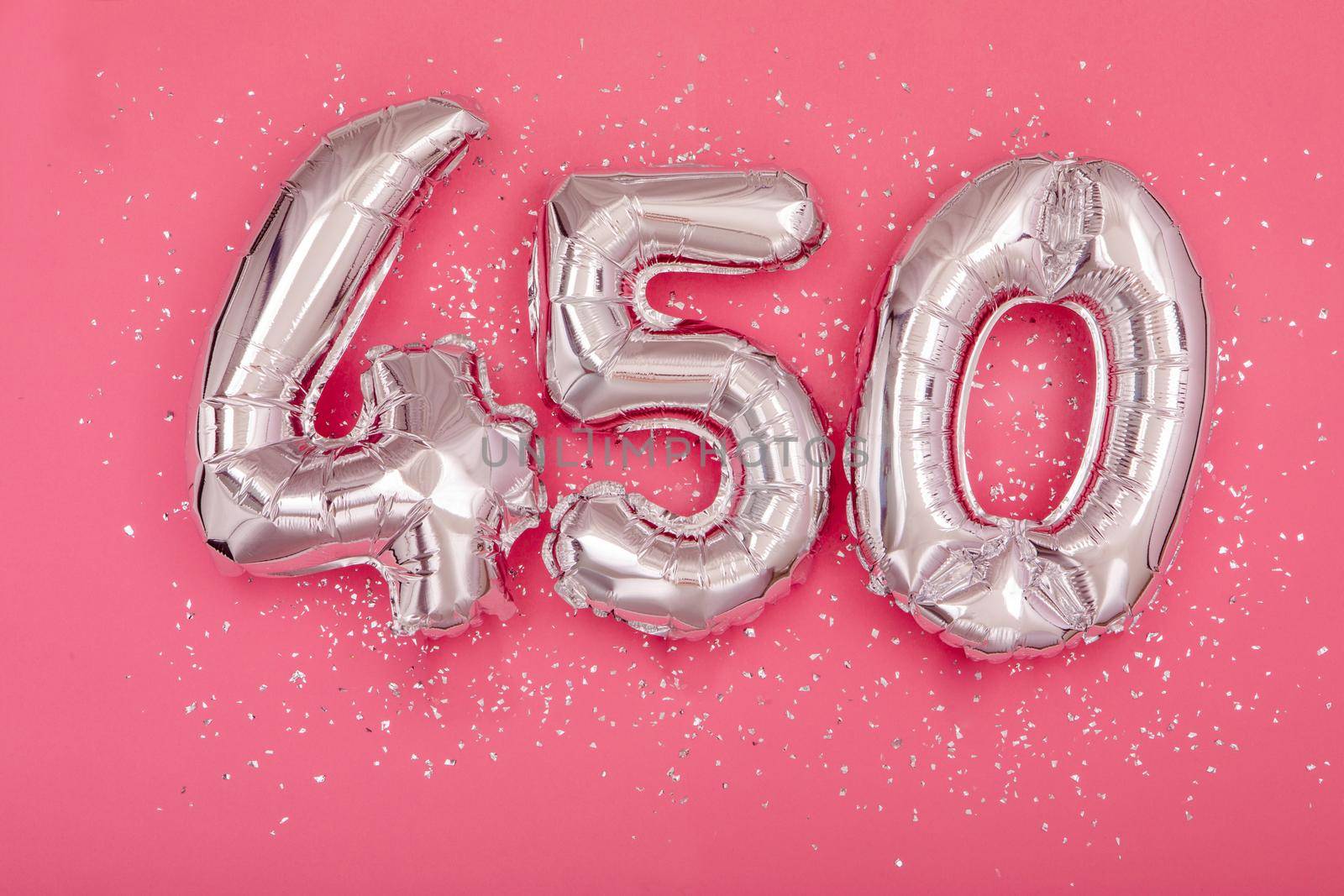 From above of silver shiny balloons demonstrating number 450 four hundred and fifty pink background with scattered glitter