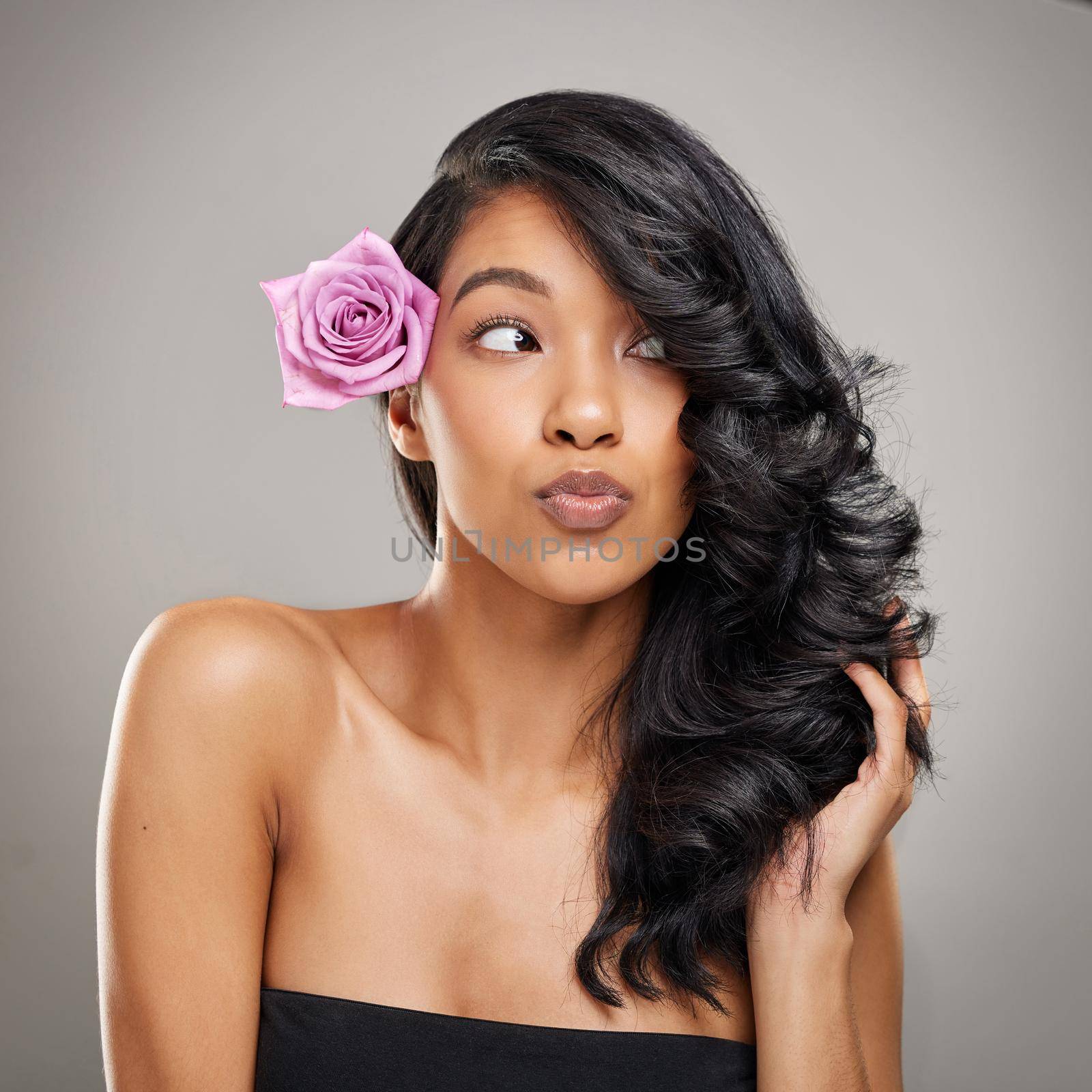 Watch out, Im unstoppable on a good hair day. Shot of a beautiful young woman posing with a flower in her hair. by YuriArcurs