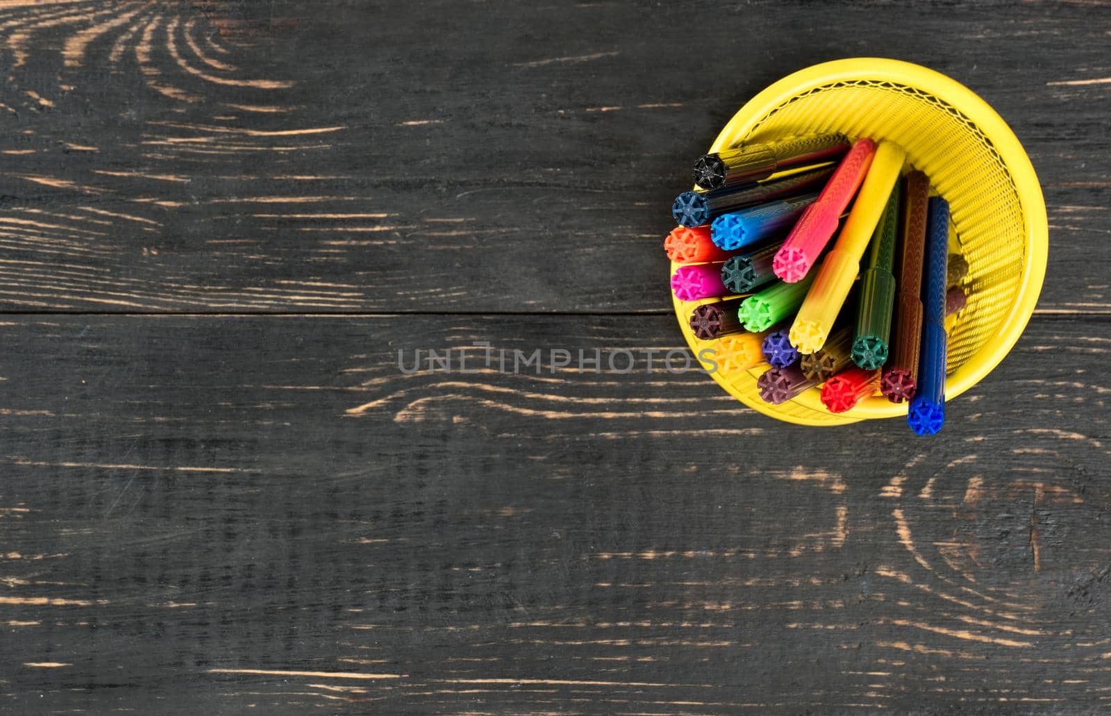 Colored markers in the empty basket on wooden background, top view